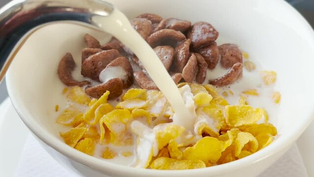 Healthy Breakfast Concept - Hand adds hot milk to a mixture of Cereal and Chocos from pot