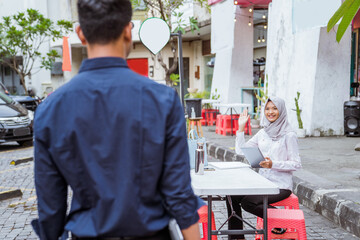 veiled girl working with tablet and waving when boyfriend comes to cafe