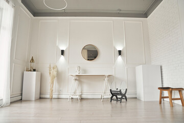 A white living room with a mirror, lamps on the wall next to a table. Part of the interior with copy space.High quality photo