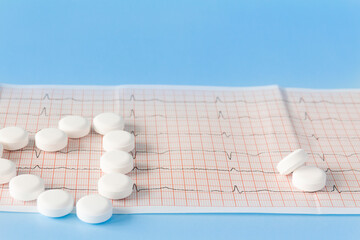 A heart made of large, white drugs on an electrocardiogram of the heart, on a blue background. The concept of a healthy lifestyle and timely medical examination.
