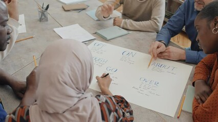 High angle view of ethnically diverse young and mature immigrants learning phrasal verbs while making educational poster