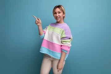 smiling blond young woman in a striped sweater points to an empty space on a blue background