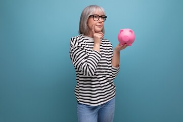 ingenious grandmother middle-aged woman has an idea where to invest her savings from a piggy bank on a bright background with save space - obrazy, fototapety, plakaty