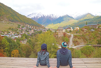 Fototapeta na wymiar Couple Relaxing at the Viewing Deck of Mestia Town with the Amazing Svan Tower-houses, Svaneti Region, Georgia