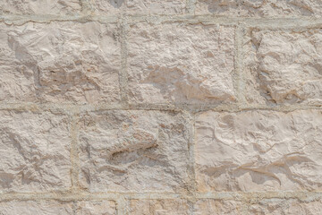 Light cream texture of the wall surface, built of rectangular natural bricks with even seams between them. Real rough surface of stone blocks of delicate color