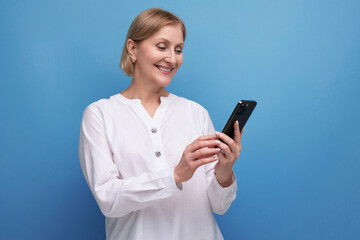pensive slender blondie middle-aged woman in a white blouse masters the smartphone gadget