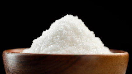 Fototapeta na wymiar White table salt falling in wooden bowl, close up