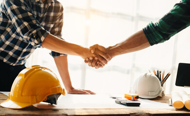 Construction team shake hands greeting start new project plan behind yellow helmet on desk in office to consults about their building project..