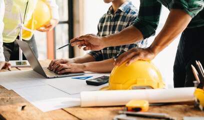 three colleagues discussing data working and tablet, laptop with on on architectural project at construction site at desk in office.
