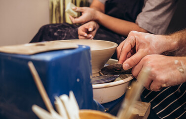 partial view of young african american couple in aprons sculpting pot on wheel with wet sponge in pottery