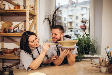 Mid adult couple smiling while doing creative painting on bowls in pottery workshop