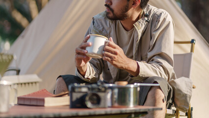 Asian man drinking coffee enjoying camping outdoors in nature. Man traveler hands holding cup of coffee.