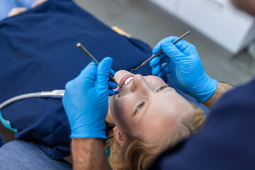 Over the shoulder view of a dentist examining a patients teeth in dental clinic. Female having her teeth examined by a dentist.