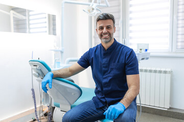 Male dentist posing at clinic over modern cabinet, empty space. Portrait shot of a young smiling...
