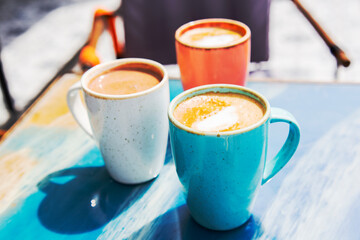 Coffee and hot chocolate in three colorful  cups on blue table in sunny day outdoors