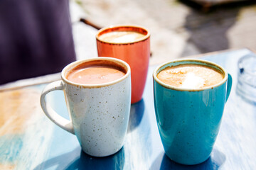 Coffee and hot chocolate in three colorful  cups on blue table in sunny day outdoors