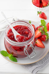 Strawberry jam in the glass jar with fresh berries on a white wooden table. Summer dessert. Copy space.