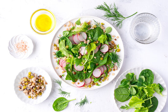 Healthy diet salad for lunch with many types of cereals and legumes (barley, lentils, beans, peas), baby spinach, green leaves and herbs, seasoned with olive oil, white background, spring and summer 