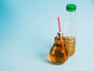 Half empty plastic bottle with drink and juice in glass reusable bottle on blue background. Concept of earth day, zero waste and plastic recycling.
