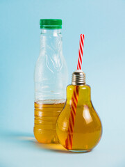 Half empty plastic bottle with drink and juice in glass reusable bottle on blue background. Concept of earth day, zero waste and plastic recycling.
