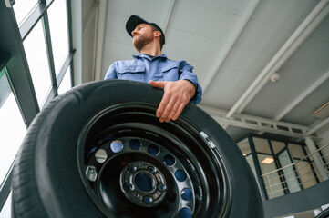 With big new tire for a change. Man in blue uniform is working in the car service