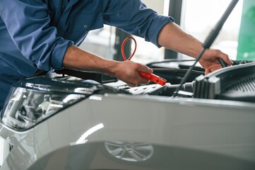 Testing breakage by using electrical terminals. Man in blue uniform is working in the car service
