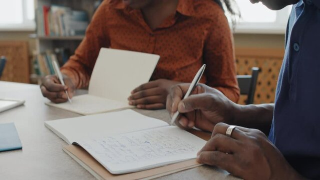 Selective focus close-up shot of senior Black man attending language class for immigrants writing essay in copybook
