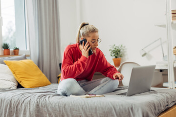 Obraz premium A young Caucasian woman is talking on the phone and sitting on the bed