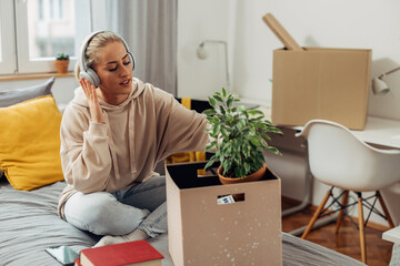 A young Caucasian woman is unpacking her things from a box while listening to music
