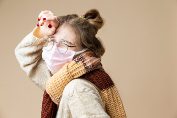 Caucasian Blond Female Girl in Round Glasses Wearing Warm Knitted Sweater Using Viral Facial Protective Mask Against Beige.