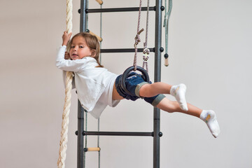 Portrait of Smiling Relaxing Caucasian Little Girl Exercising on Thewall-bars Indoor at Wall Bars.
