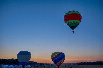 Line of Colorful Air Balloons Levitating Over the Field Outdoor On Clear Blue Evening Sky At Twilight.