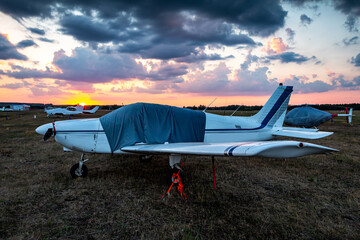 Covered airplanes and helicopters of small aviation at the airfield at picturesque sunrise
