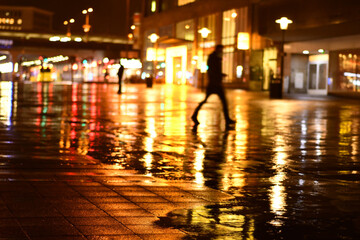 Man walks in the dark in the rain at the station forecourt in Essen, Germany - obrazy, fototapety, plakaty