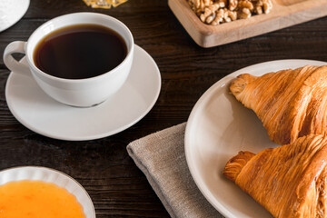 Coffee cup with croissant on a rustic dark wooden table. Food series. Two tasty fresh croissants, jam, orange juice. Continental breakfast served with freshly baked pastry. Close up view, Good morning