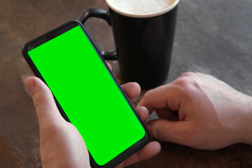Man Use of Mobile Phone with Blank Green Screen in Cafe on Rustic Vintage Wooden Table. Male Holding Smart Phone Empty ChromaKey Screen Mock up in Coffee Shop. Morning. Showing Mock up Video