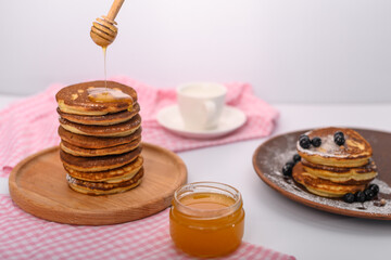 a stack of pancakes on a wooden tray and a jar of honey.