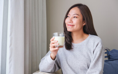 Portrait image of a young woman holding and showing a glass of fresh milk