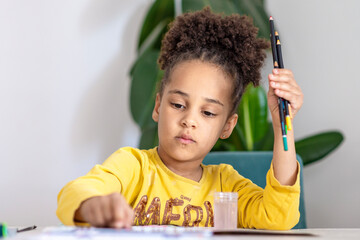 Beautiful girl playing on her own, developing artistic skills. Childhood, creativity and art concept - little African American girl drawing pictures with acrylic wooden crayons on paper at home.