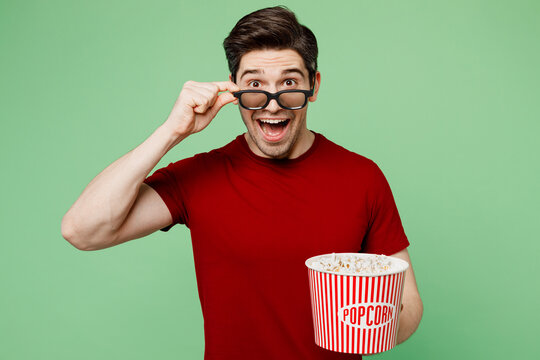 Young shocked fun surprised impressed amazed man lower 3d glasses wear casual clothes watch movie film hold bucket of popcorn in cinema isolated on plain pastel light green background studio portrait.