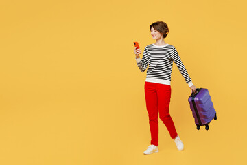 Traveler woman wears casual clothes hold suitcase mobile cell phone isolated on plain yellow color...