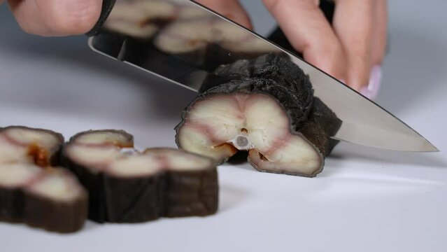 Close-up view 4k stock video footage of tasty cooked smoked eel fish. Woman cuts fish on white plastic chopping board background using knife