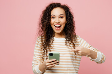 Young surprised shocked woman of African American ethnicity she wear light casual clothes hold in hand use point finger on mobile cell phone isolated on plain pastel pink background studio portrait.