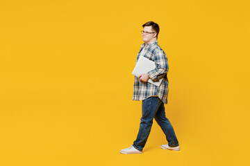 Full body side view young IT man with down syndrome wear glasses casual clothes hold closed laptop...