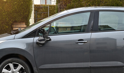 A damaged car is parked on the shoulder of the road with a broken side mirror.