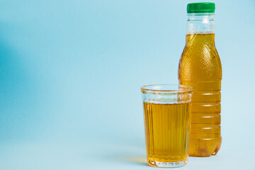 Glass of juice and plastic bottle on blue paper background. Concept of earth day, zero waste and plastic recycling.