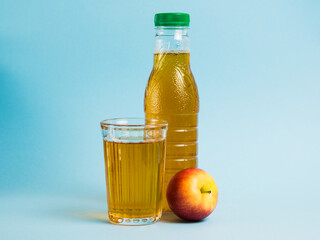 Apple juice drink in plastic bottle and reusable glass cup on blue paper background. Concept of earth day, zero waste and plastic recycling.
