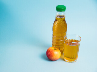 Apple juice drink in plastic bottle and reusable glass cup on blue paper background. Concept of earth day, zero waste and plastic recycling.