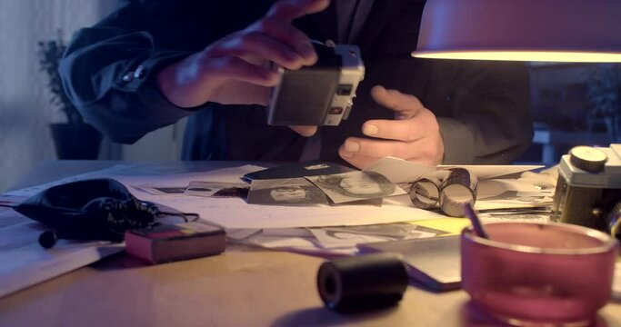 The hands of a forensic scientist are examining cameras at the table. He takes the camera, smokes a cigarette. Learn to understand technology before observing. CZ, Kladno, Polska, 8.3.23