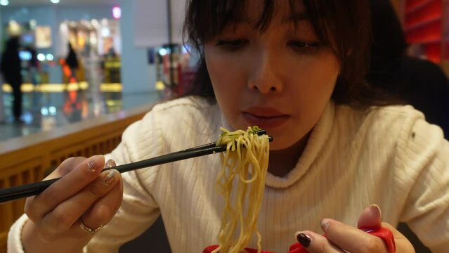An attractive Asian woman is having dinner at the restaurant, eating ramen or Japanese noodle using chopstick